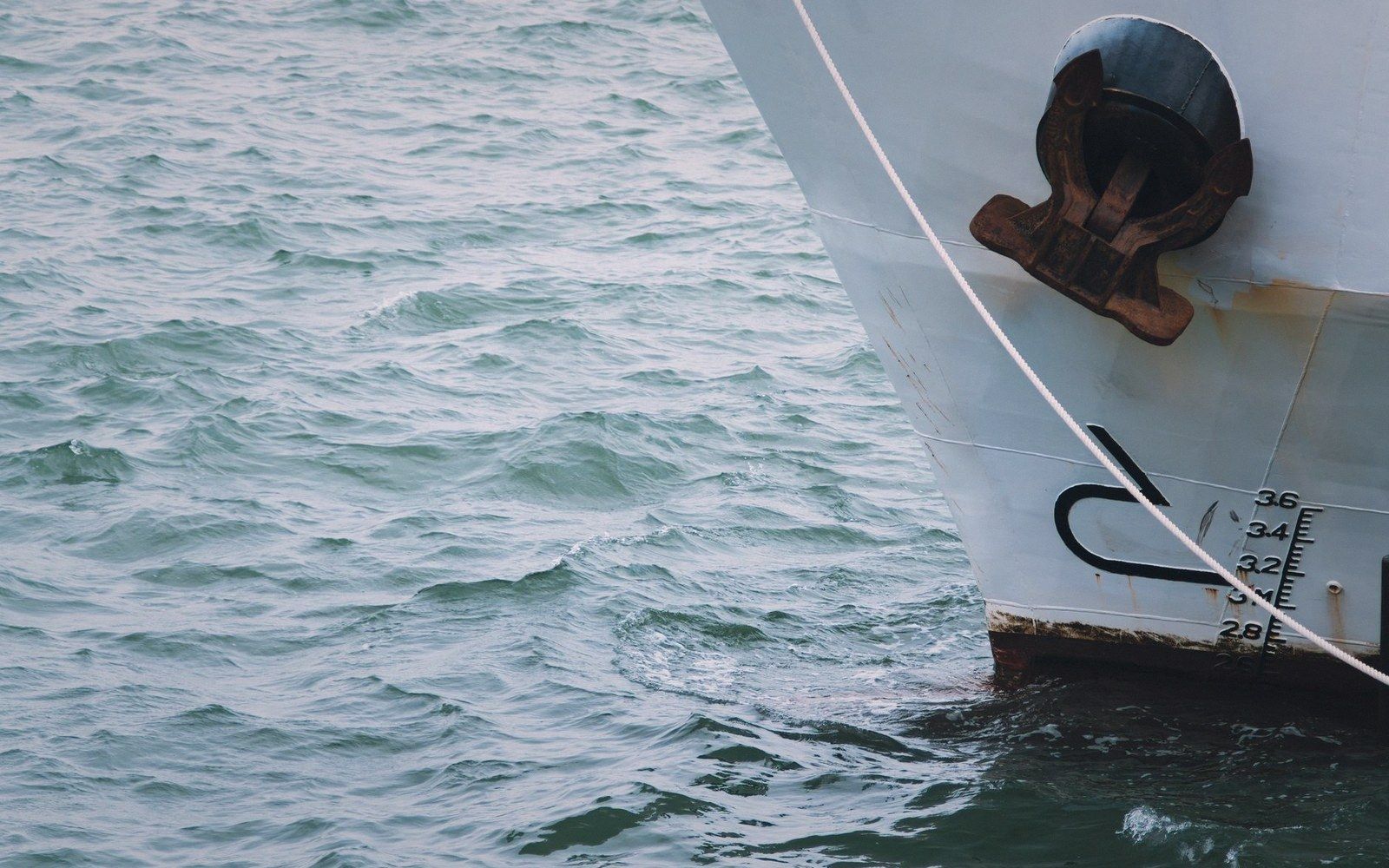 White ship's bow with a rusty anchor and draft marks against calm water