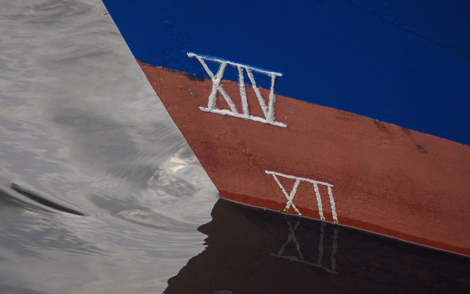 Roman numeral draft marks on a ship's bow reflected in calm water