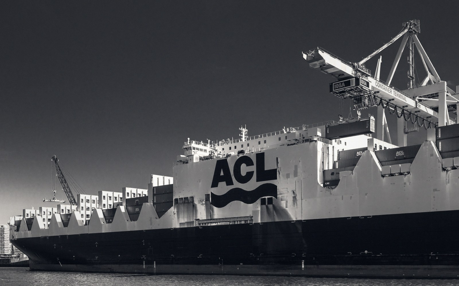 An ACL container ship docked at a port terminal beneath a large gantry crane