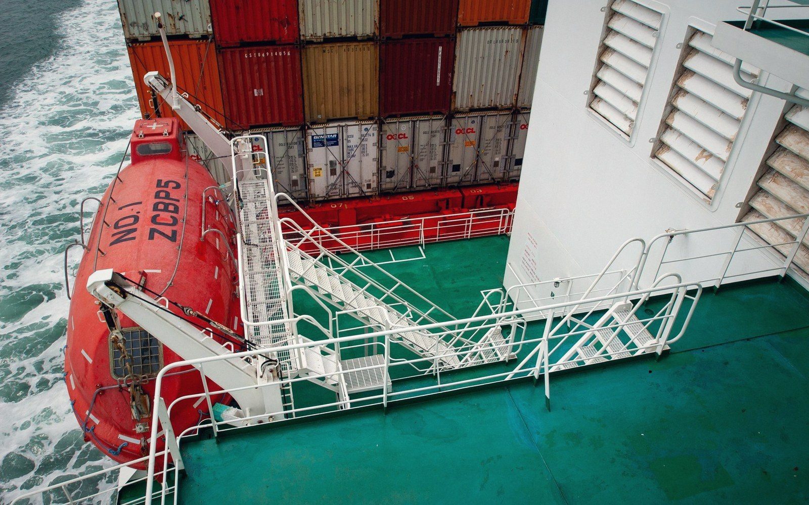 An enclosed lifeboat and stairways on a container ship's deck viewed from above