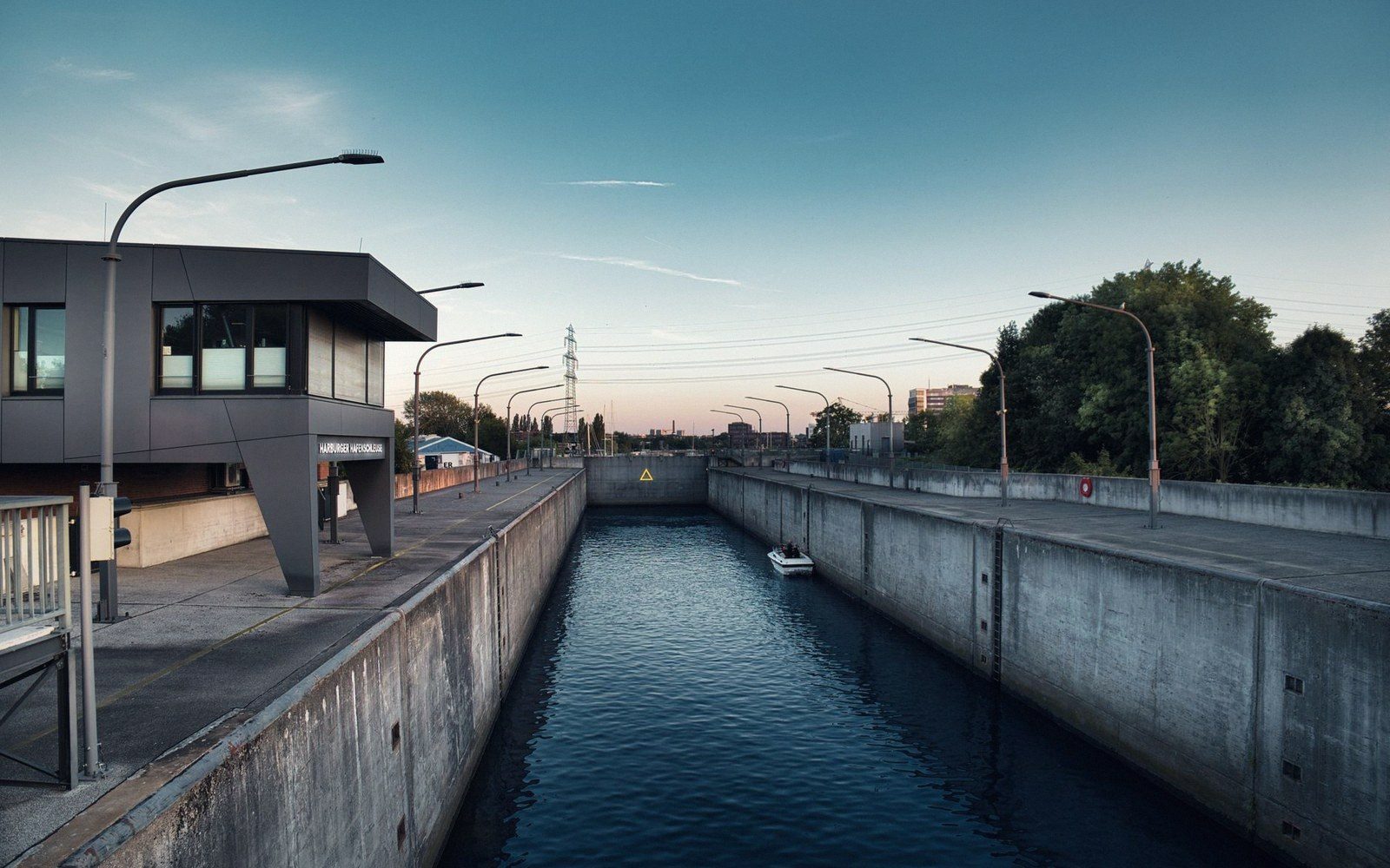 A small boat passes through a concrete canal lock beside a control building at dusk