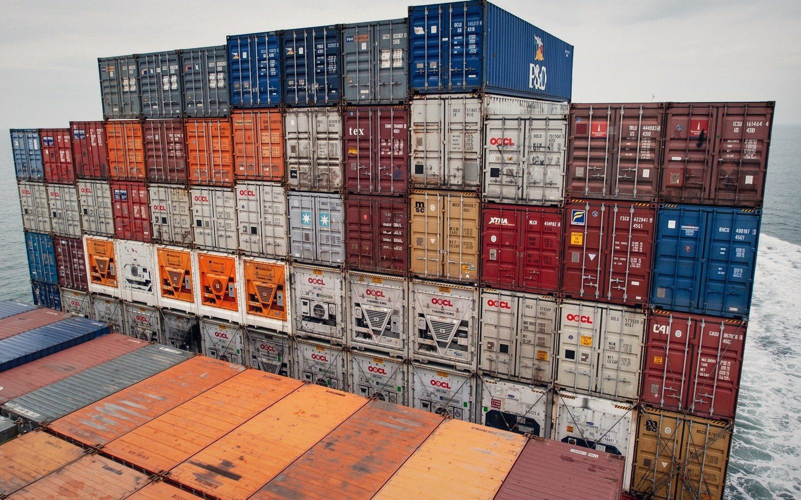 Container stack on a laden ship photographed from deck level looking straight up, boxes receding to a strip of sky